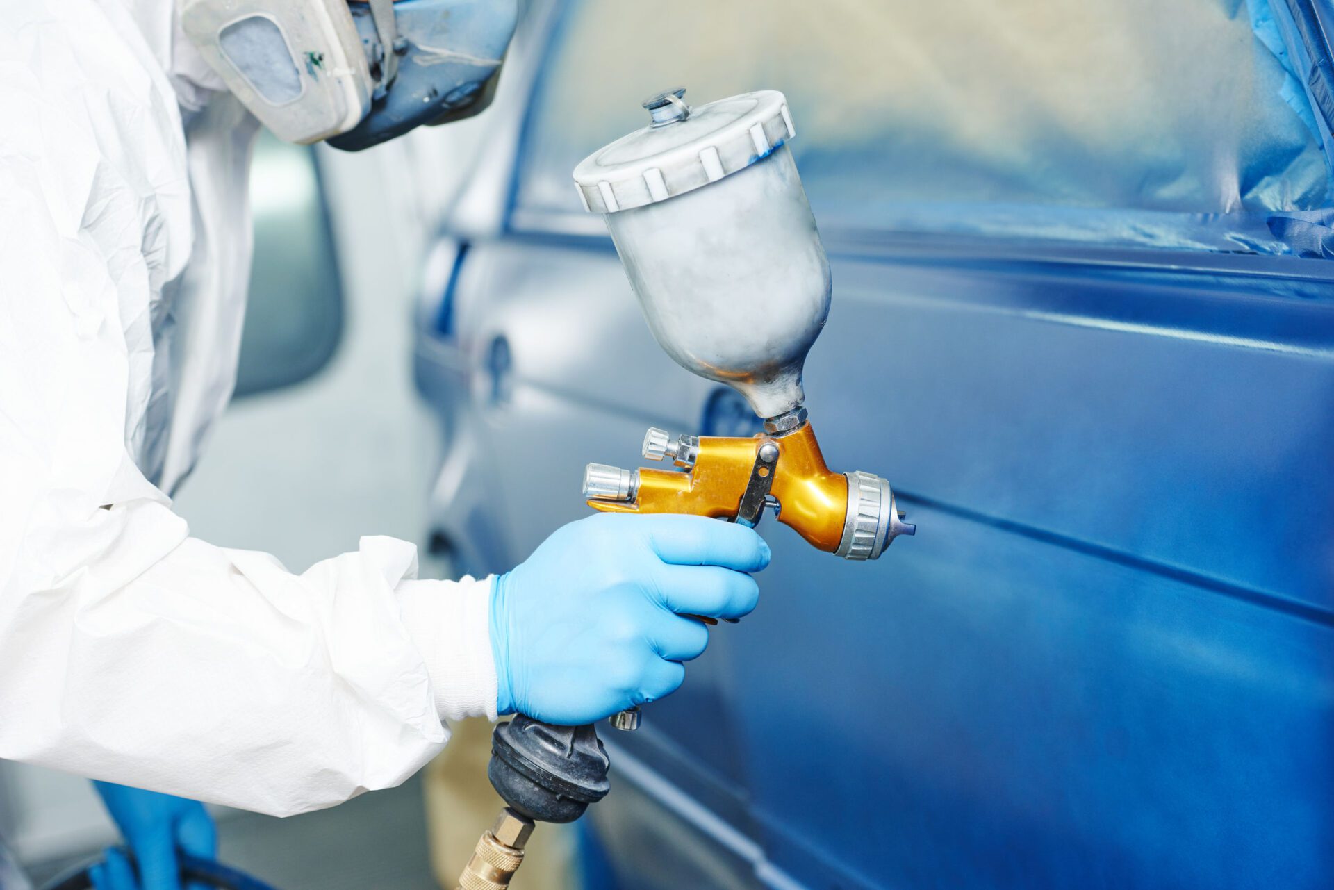 automobile repairman painter hand in protective glove with airbrush pulverizer painting car body in paint chamber